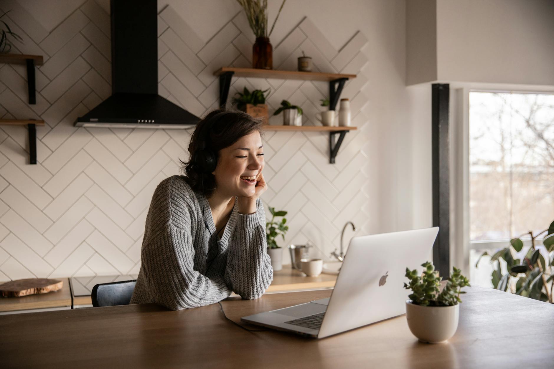 smiling woman talking via laptop in kitchen